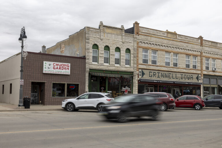 Historic downtown Grinnell, Iowa storefront with passing vehicles and traditional architecture.