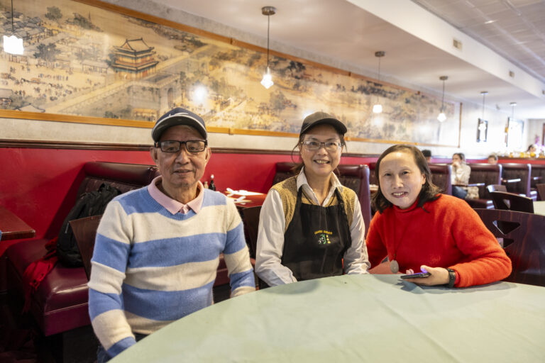 Three people posing in a red booth at an Asian restaurant with decorative mural.